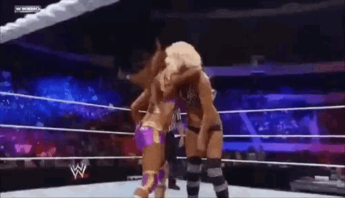 two women are wrestling in a wrestling ring and one of them is wearing a purple outfit .