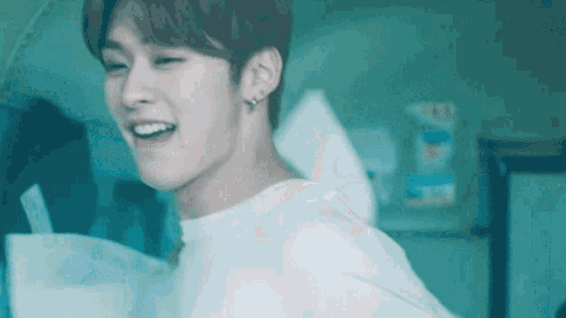 a young man wearing a white shirt and earrings is smiling and looking at the camera .