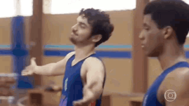 two men are standing next to each other in a gym . one of the men is doing a trick on the floor .