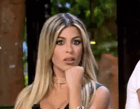 a woman with blonde hair is holding her fist to her chin and making a surprised face .