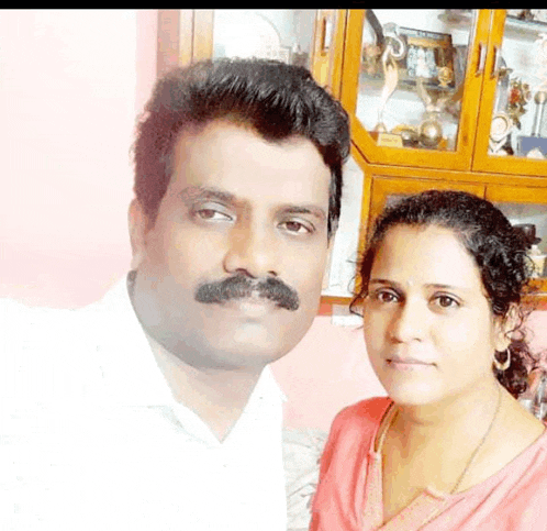 a man and a woman pose for a picture in front of a cabinet