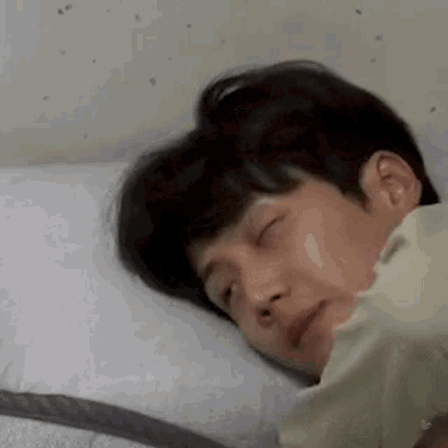 a young man is sleeping on a bed with his eyes closed and his head on a pillow .