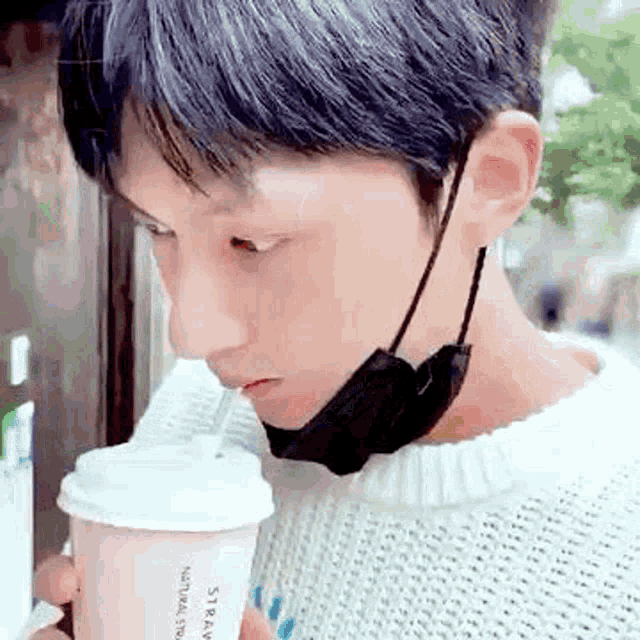 a young man wearing a mask is drinking from a cup .