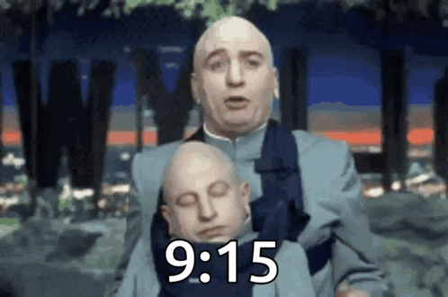 a bald man is holding a smaller bald man in his arms with the time 9:15