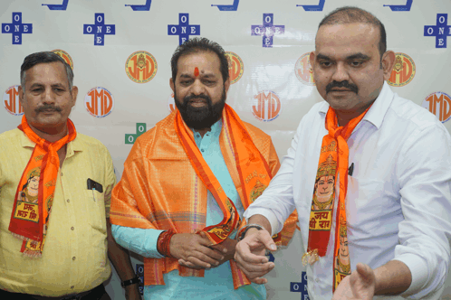 a man wearing an orange scarf with a picture of a goddess on it stands next to two other men