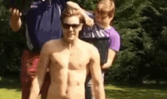 a shirtless man wearing sunglasses is standing next to a boy .