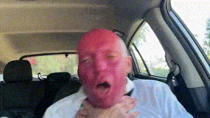 a man with red face is sitting in the back seat of a car .