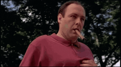 a man in a red shirt is smoking a cigar and looking at the camera .