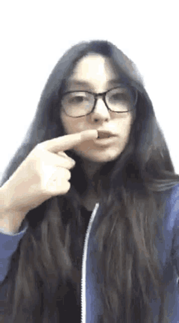a girl wearing glasses and a blue jacket is pointing at her face .