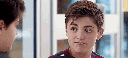 a young boy is making a funny face while talking to another boy in a room .
