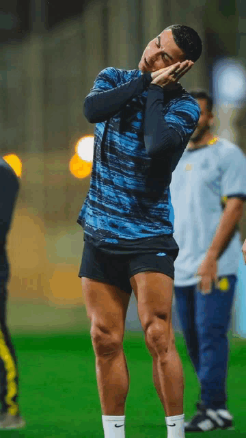a man in a blue shirt and black shorts holds his hands to his face