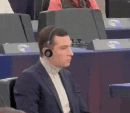 a man wearing a suit and headphones sits in a row of chairs
