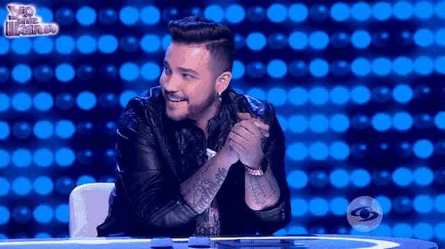 a man with a tattoo on his arm sits at a table in front of a yo me llamo sign