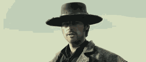 a man wearing a cowboy hat and a leather jacket is standing in the desert .