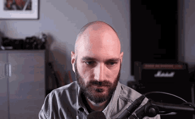 a bald man with a beard is sitting in front of a marshall amp