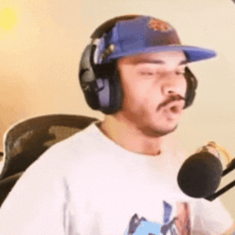 a man wearing headphones and a hat is standing in front of a microphone .