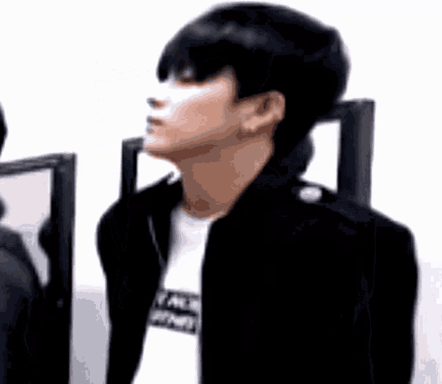 a man wearing a black jacket and a white shirt is standing in front of two mirrors .