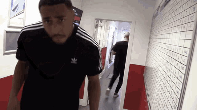 a man wearing a black adidas shirt stands in a hallway