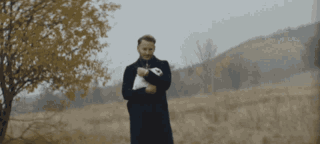 a man in a black coat is holding a small white rabbit