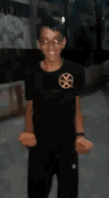 a young man wearing glasses and a black shirt with a gold circle on the front