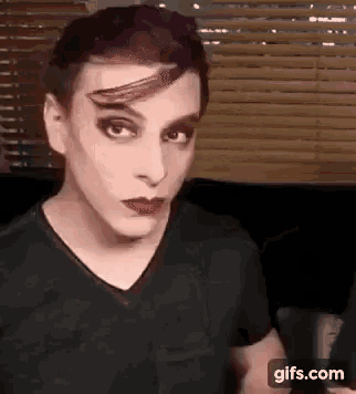 a man with purple hair and red lipstick is wearing a black shirt and making a funny face .