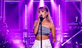 ariana grande is singing into a microphone on stage in front of a purple background .