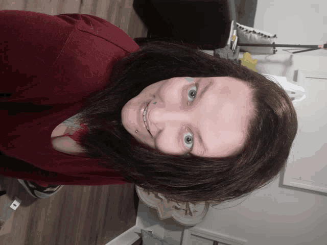 a woman with a tattoo on her face is smiling and wearing a red sweater