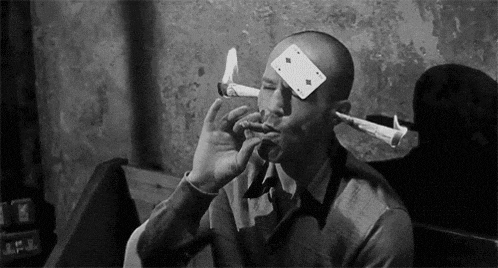 a man is smoking a cigar with a playing card on his forehead and a syringe in his mouth .