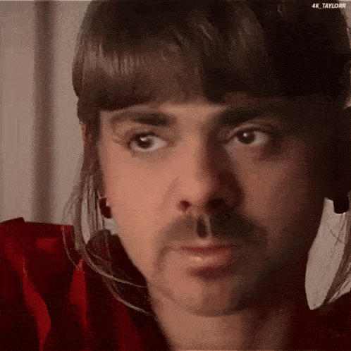 a close up of a man 's face with a mustache and fringe .