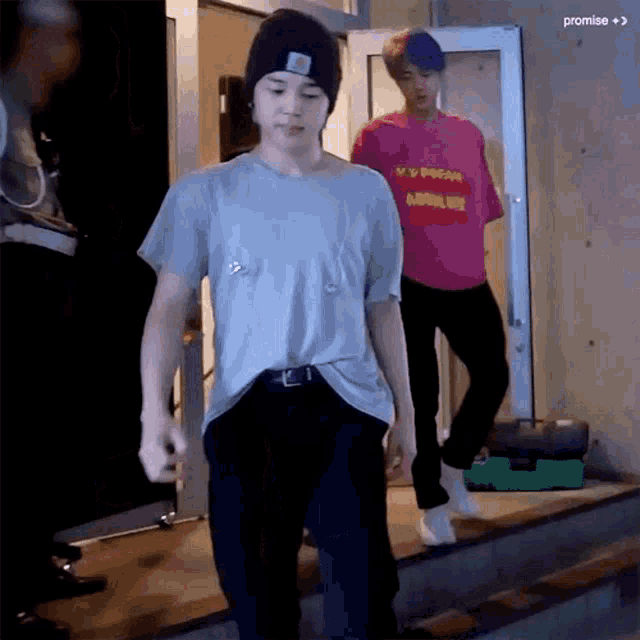 a man in a pink shirt is walking down stairs next to a man in a gray shirt .