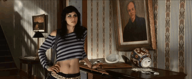 a woman in a striped crop top stands in front of a painting of a man