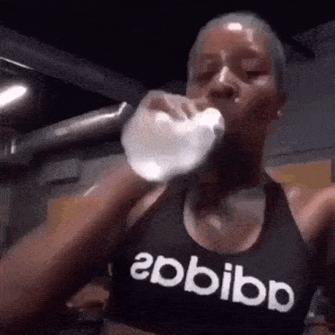 a woman wearing an adidas tank top is drinking water from a bottle