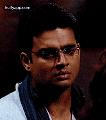 a man wearing glasses and a scarf is looking at the camera .
