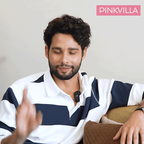 a man with a beard is sitting on a couch with a pinkvilla logo in the corner