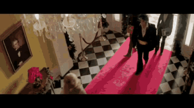 a man is walking down a red carpet in a room with a checkered floor .