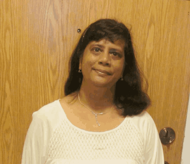 a woman stands in front of a wooden door wearing a white shirt