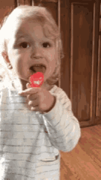 a little girl is holding a red heart shaped lollipop in her hand