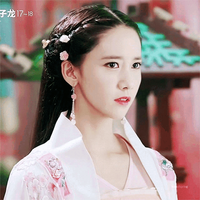 a woman wearing a pink and white kimono with flowers in her hair looks at the camera