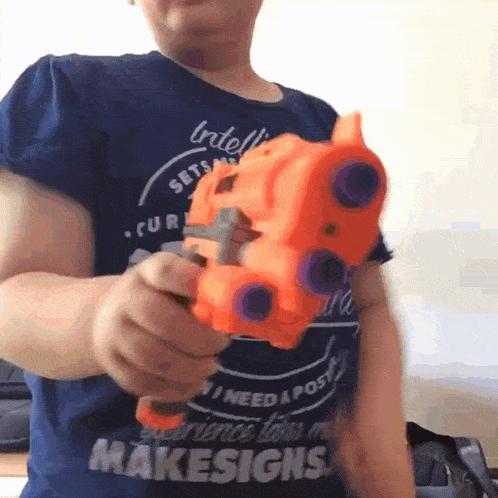 a person wearing a blue shirt that says " makesigns " is holding a toy gun