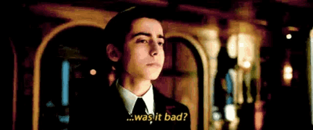 a young man in a suit and tie is standing in a dark room and talking to someone .