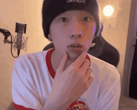 a young man wearing a beanie and a white t-shirt is sitting in front of a microphone .