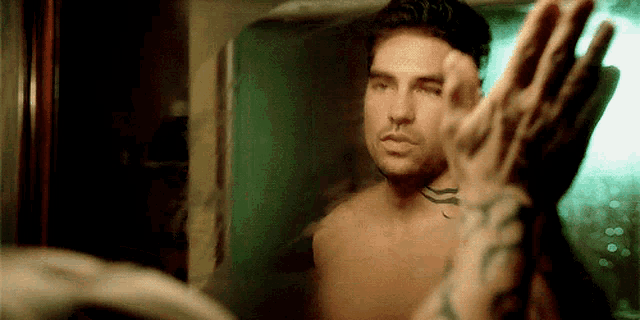 a shirtless man looks at himself in a mirror