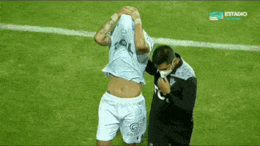 a man wearing a mask is helping a soccer player with his head in his hands on a field .