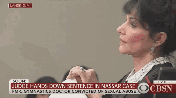 a woman in a judge 's robe holds a piece of paper in front of a screen that says cbsn live