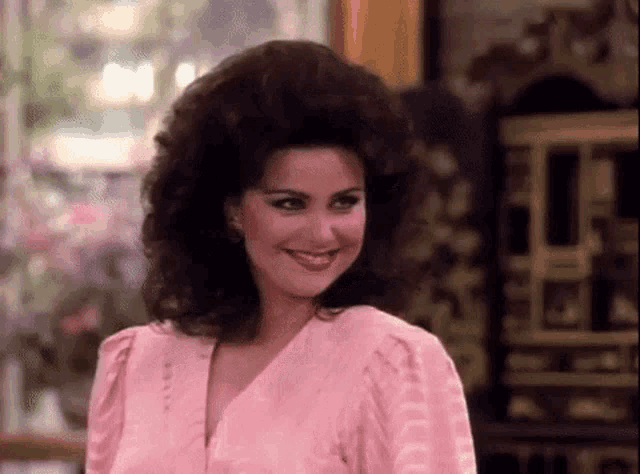 the woman is wearing a pink shirt and has a big hairdo .