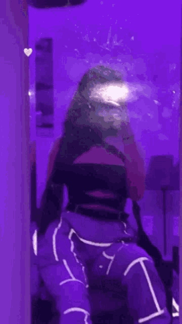 a woman is taking a selfie in front of a mirror with a purple light behind her .