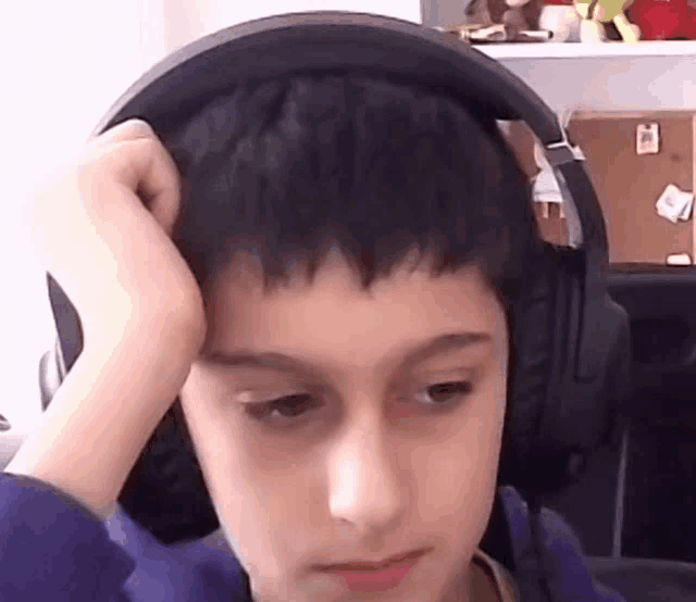 a young boy wearing headphones looks at the camera with his hand on his head