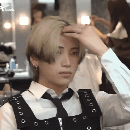 a man in a white shirt and black tie adjusts his hair with a x labels logo in the background