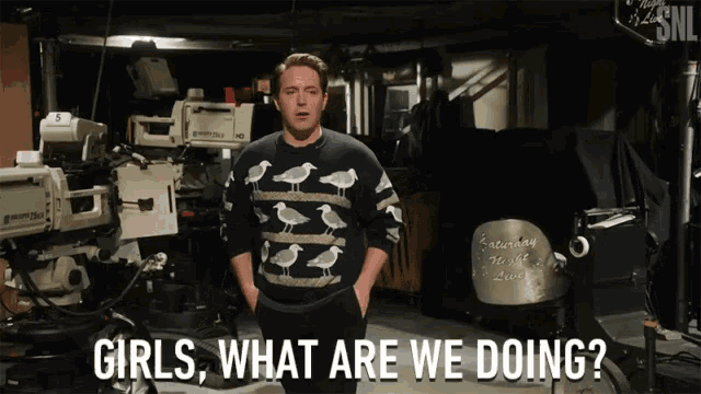 a man wearing a sweater with seagulls on it stands in front of cameras and says " girls what are we doing "