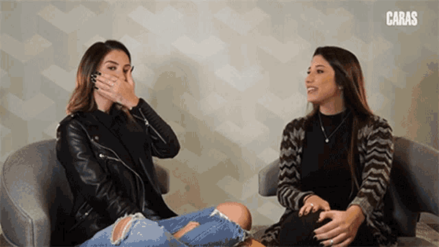 two women are sitting in chairs and one is covering her mouth with her hand and the word caras is above them